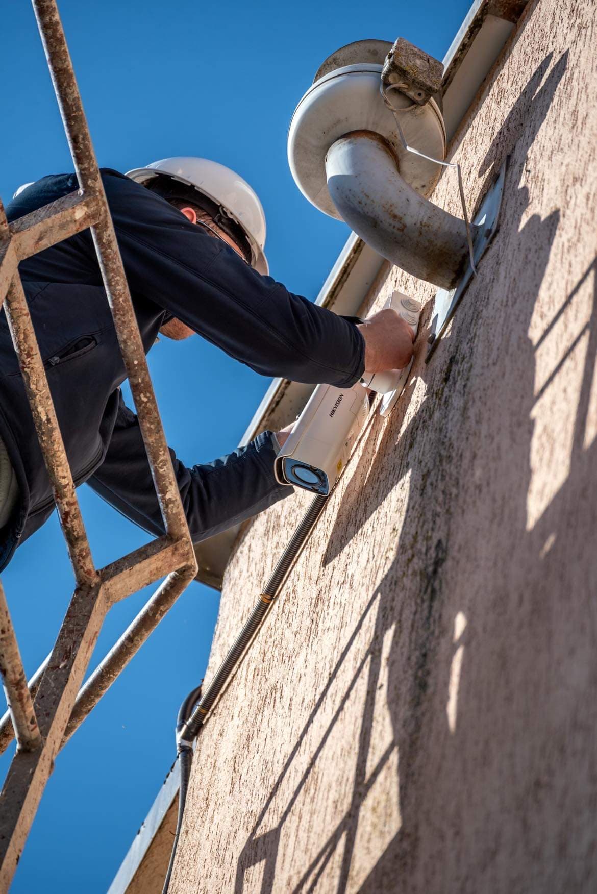 Technikas montuoja Hikvision vaizdo stebėjimo kamerą ant pastato sienos
